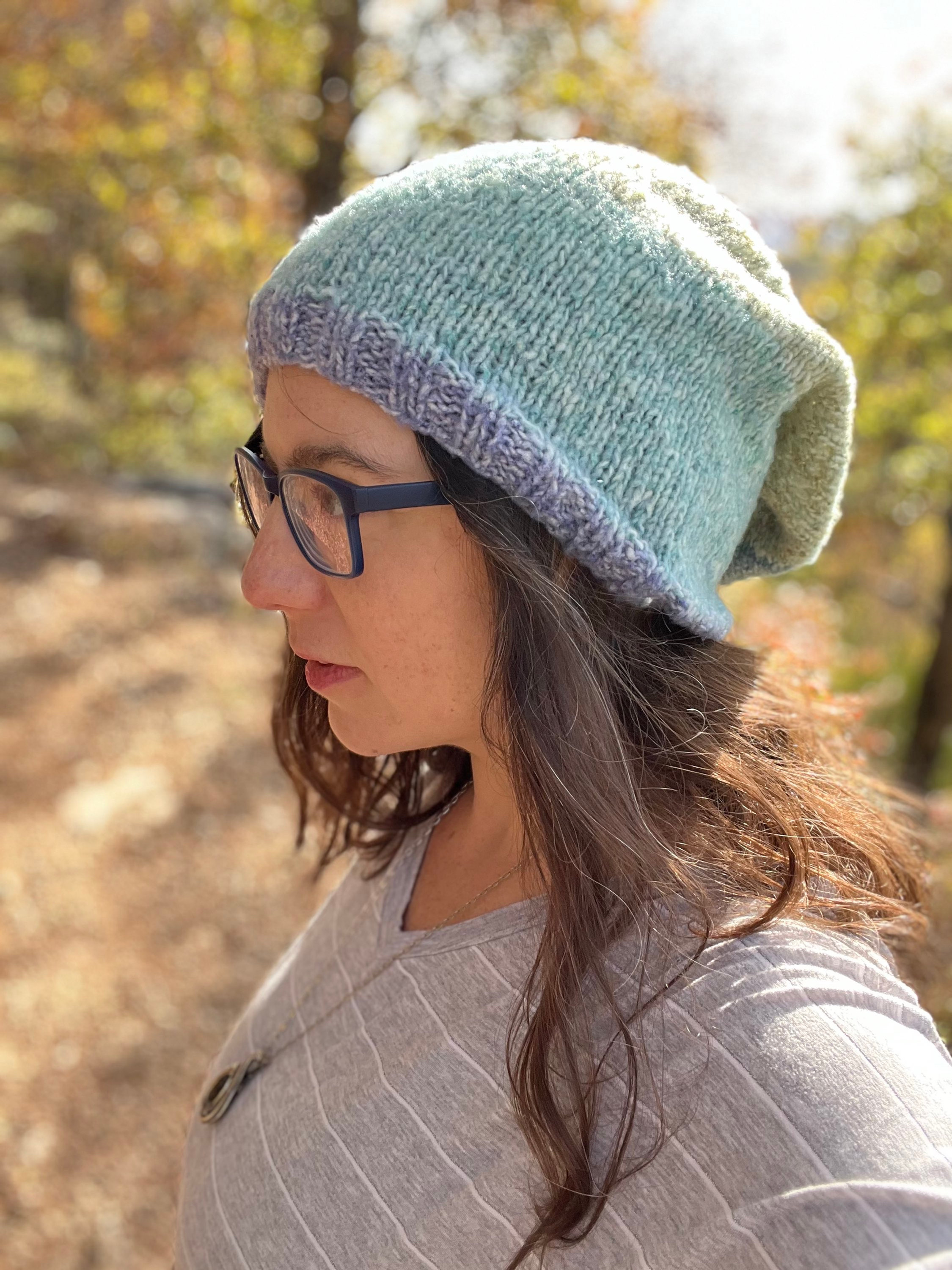 Brunette woman in glasses wearing slouchy hat with forest background