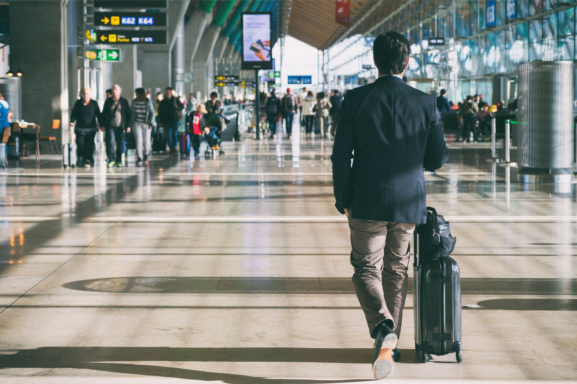 Business traveler walking through a busy airport terminal with a roller suitcase.