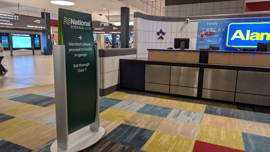 A green National Emerald Club sign near a rental counter, guiding customers to use the Emerald Aisle and skip the traditional check-in process.