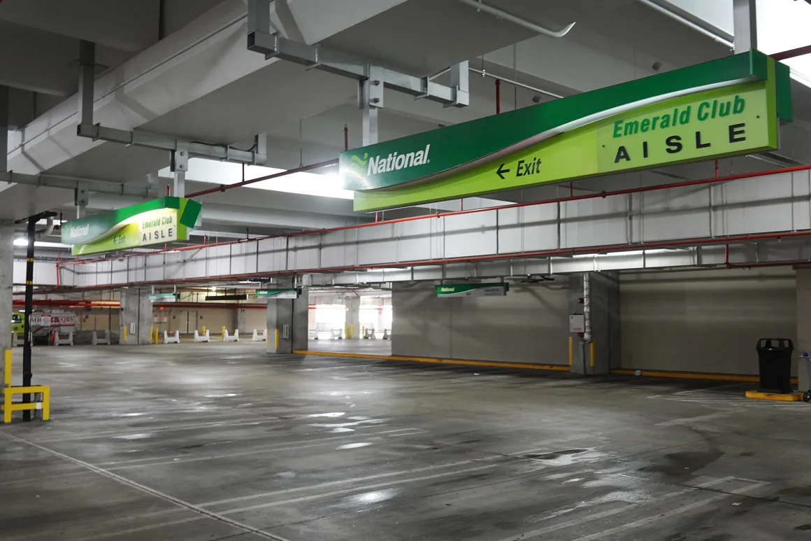 Empty Emerald Club Aisle at an airport rental garage, with bright green overhead signage for National Car Rental directing premium members.