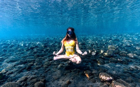 Femme en maillot jaune une pièce qui effectue une position de yoga dans l'eau