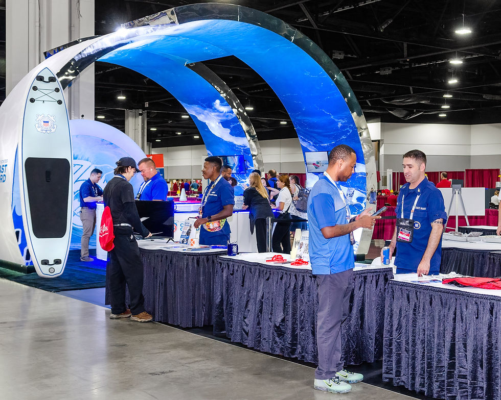 Interactive trade show exhibit with curved LED graphics, themed displays, and attendees speaking with staff and viewing demos