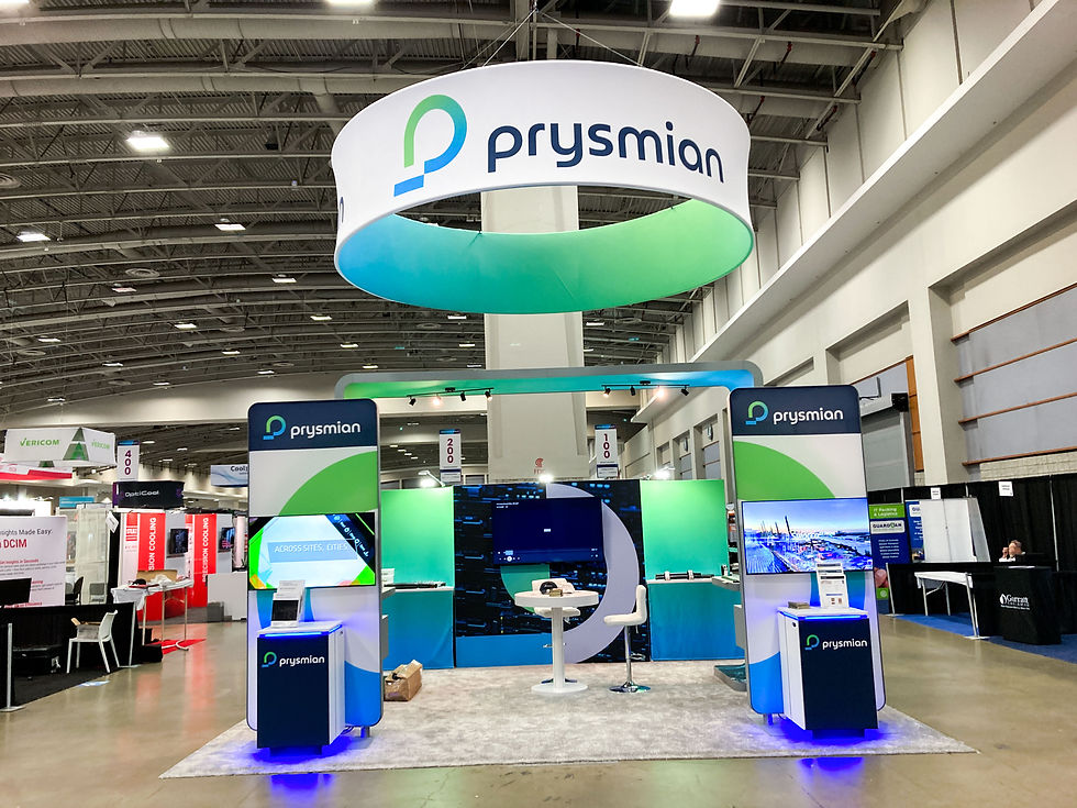 Prysmian trade show exhibit with branded hanging sign, digital displays, counters, and lighting in a large convention hall