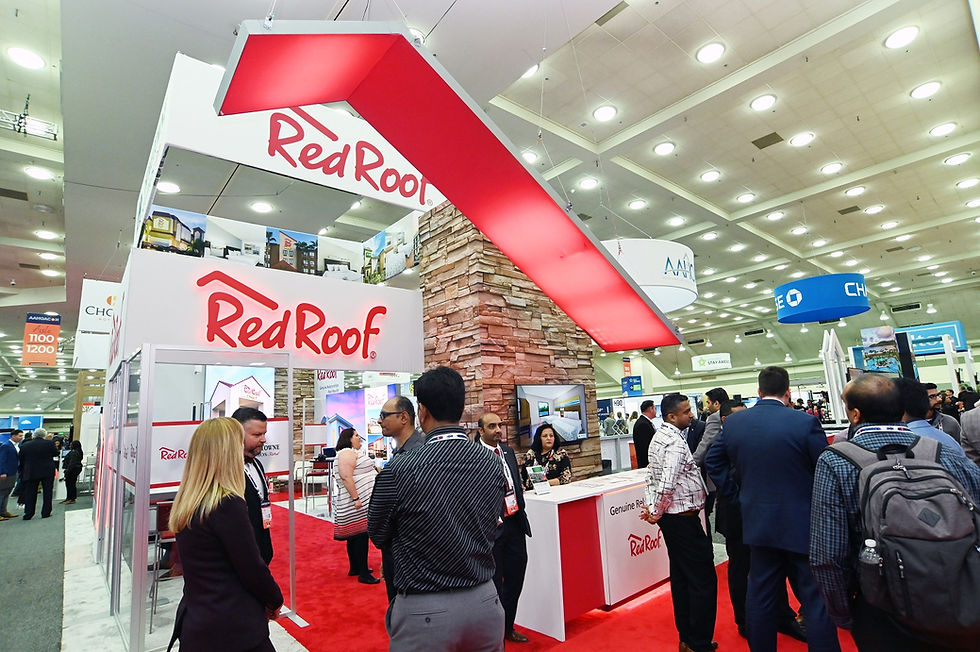 Red Roof Inn trade show booth with oversized red rooftop structure, stone chimney feature, and crowd of attendees.