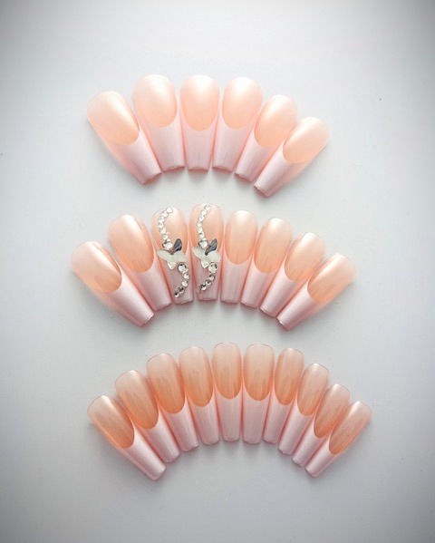 features a transparent peachy pink base classic white French tips with rhinestones and 3D butterflies