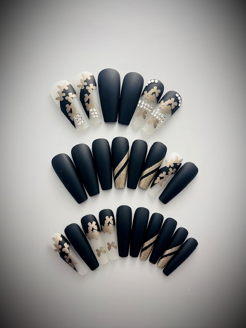 The Nora set features matte black nails with white frosted accent nails adorned with light golden butterflies and rhinestones