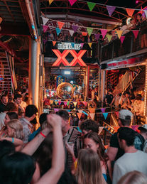 Vibrant party with dancing people, colorful flags, and an 'XX' sign