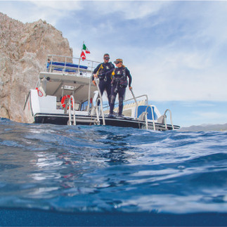 Two divers on the edge of the catamaran about to dive into the water by the Arch of Cabo, Mexico.