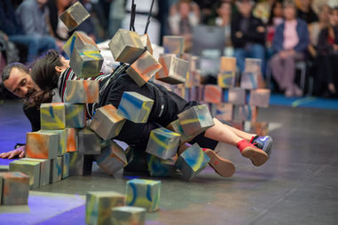 Megan Lowe and Roel Seeber crashing into a tower of foam blacks, hovering off the ground via rope and harness rock climbing equipment.