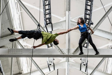Roel Seeber and Megan Lowe dancing in the ceiling beams for Fort Mason's Gateway Pavilion, suspended by rope and harness rock climbing gear.