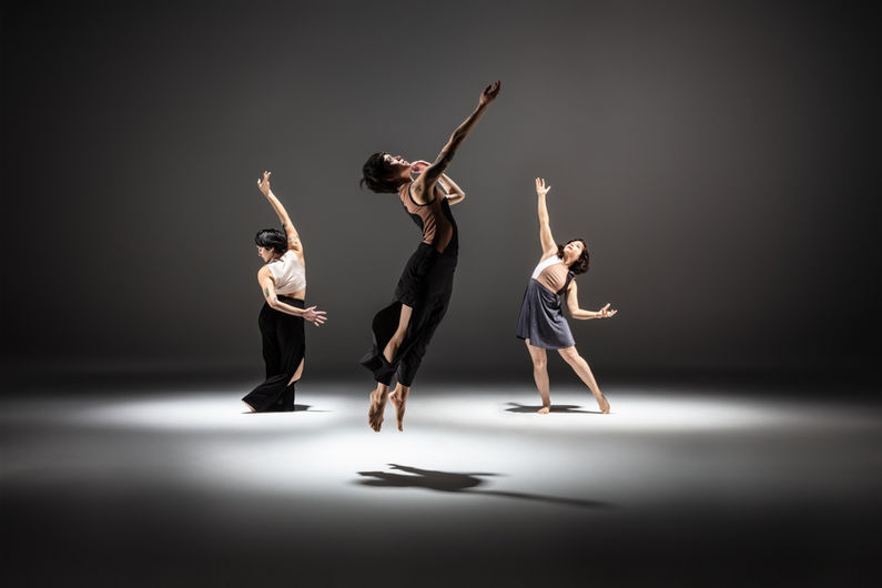 Malia Hatico-Byrne is jumping up towards the sky in the foreground, with Melissa Lewis Wong and Megan Lowe reaching towards her in the background.