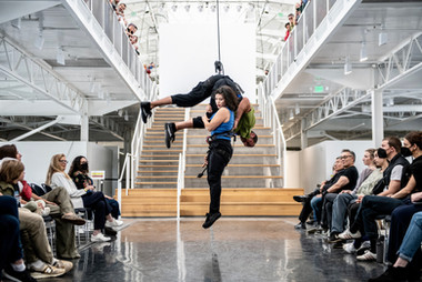 Megan Lowe hovers above the ground by holding on to Roel Seeber who is suspended by rope and harness rock climbing gear, dancing together in Fort Mason's Gateway Pavilion,