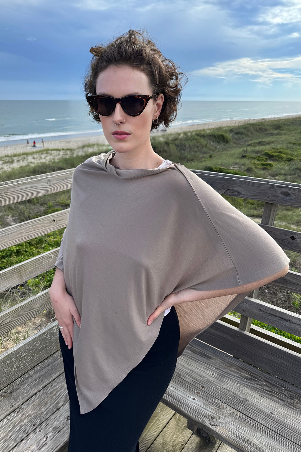 Woman wearing the burlywood Merino Summer Poncho in a relaxed lifestyle pose at the beach.