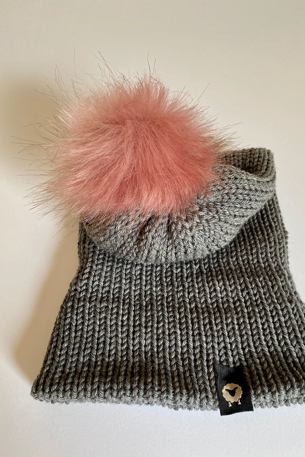 Thumbnail: Heather grey pom beanie with blush pink faux-fur pom, product shot showing knit texture and pom detail on white background.