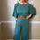 Thumbnail: Woman wearing the Sierra dusty teal rib merino jumpsuit with leather belt in a relaxed lifestyle pose.