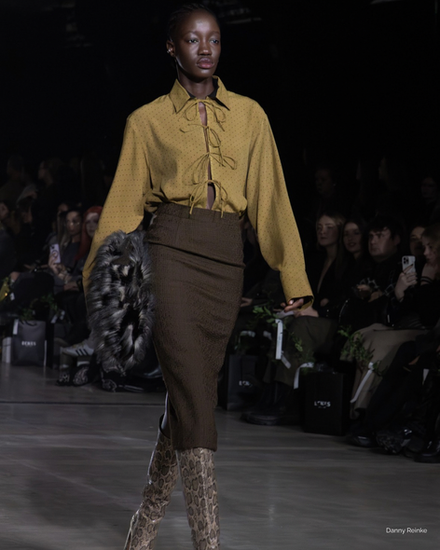 Runway model wearing a mustard lace-up blouse, brown skirt, and python boots from Danny Reinke FW26 at Berlin Fashion Week.