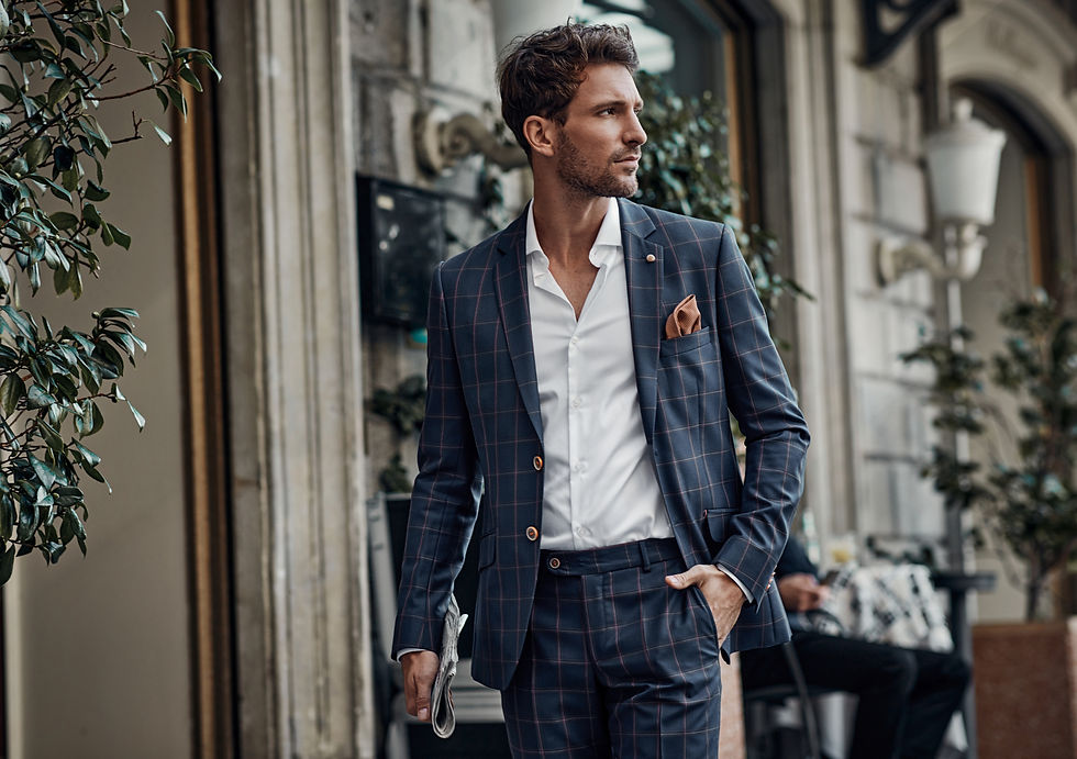 Man wearing a tailored blue suit with an open-collar shirt, standing in front of European-style stone architecture, representing modern suiting and refined confidence.