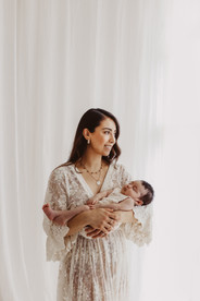 Eine Strahlende Mutter im weißen Kleid hält ihr Baby bei einem Babyshooting in Stuttgart.