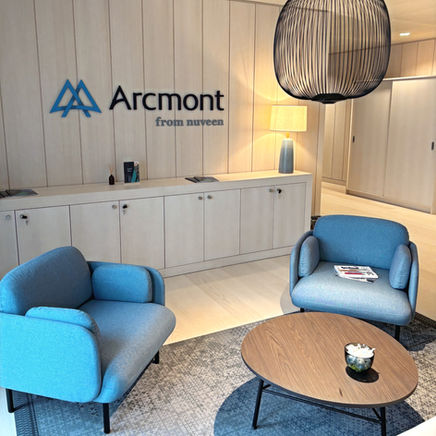 Einladender Empfangsbereich mit blauem Arcmont-Logo, zwei blauen Loungesessel und rundem Holzcouchtisch.