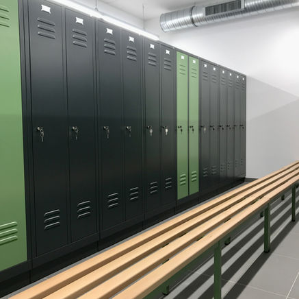 Umkleideraum mit einer Reihe dunkelgrüner und schwarzer Spindschränke mit Schlüsseln sowie einer Holzbank davor.