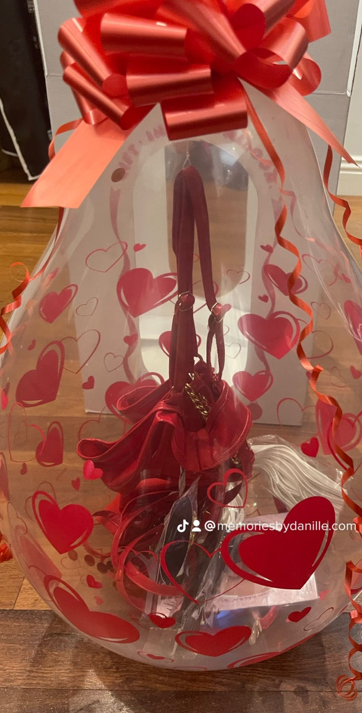 Clear balloon red bow heart prints sitting on floor.