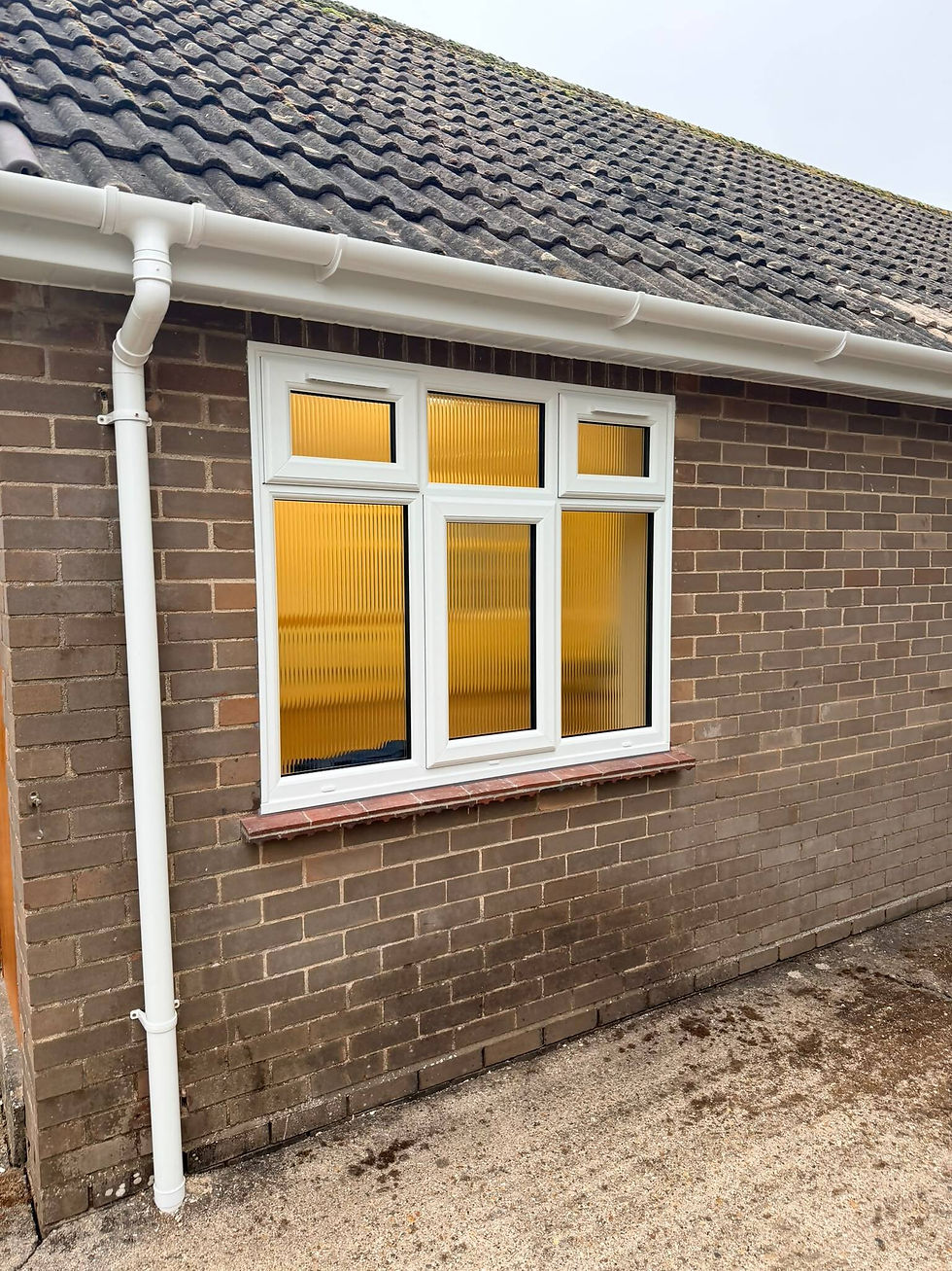 White uPVC window with yellow privacy-textured glass set into a brown brick wall beneath a tiled roof with white guttering