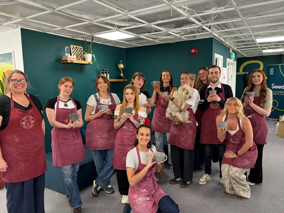 Team of colleagues hold up their finished pottery creations at a team building workshop in Brighton