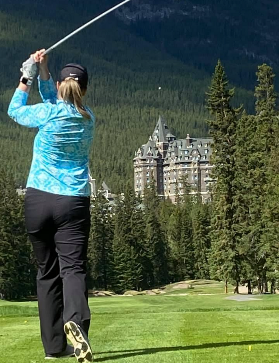 Woman playing golf with Fairmont Banff Springs in the background.