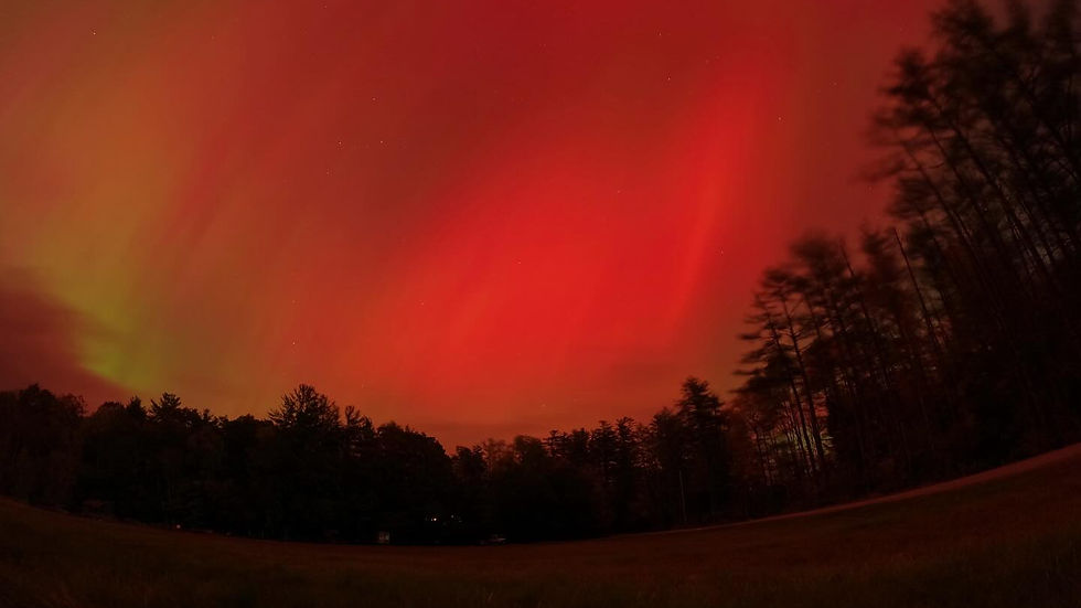 A spectacular display of the Aurora lights illuminates the night sky with vibrant red and orange hues over a serene landscape in Maine.