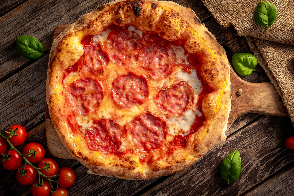 Felülről fotózott pepperónis pizza fa vágódeszkán, koktélparadicsomokkal és bazsalikommal