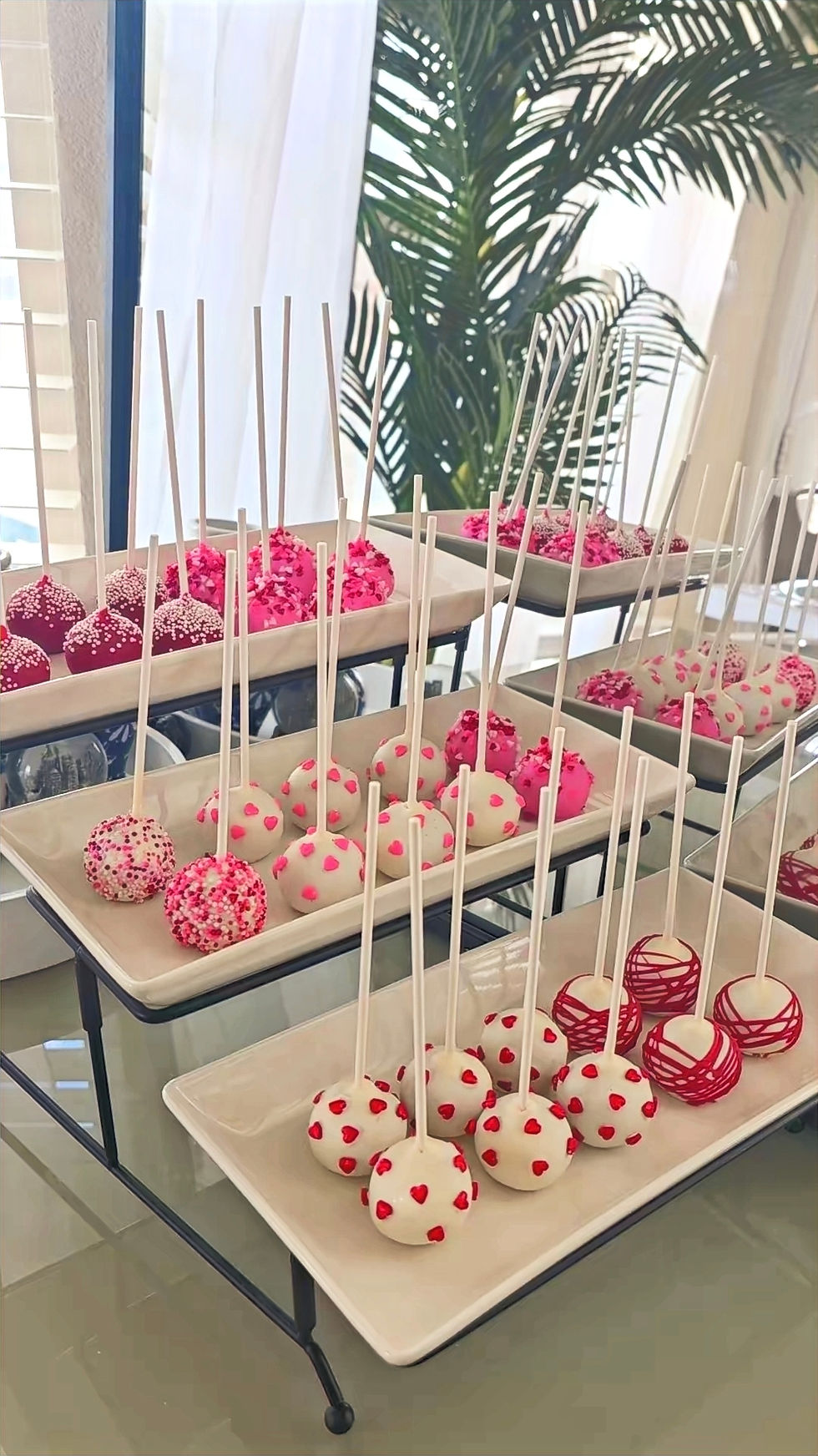 Multiple pink and white cake pops on sticks, decorated with sprinkles and dots