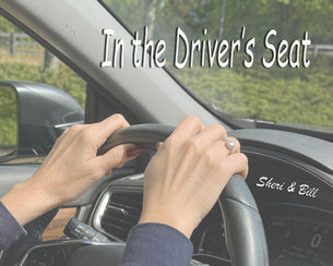 image of hands on steering wheel. text on image says in the driver's seat (original photography by Sheri & Bill)
