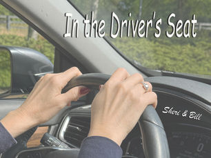 image of hands on steering wheel. text on image says in the driver's seat (original photography by Sheri & Bill)