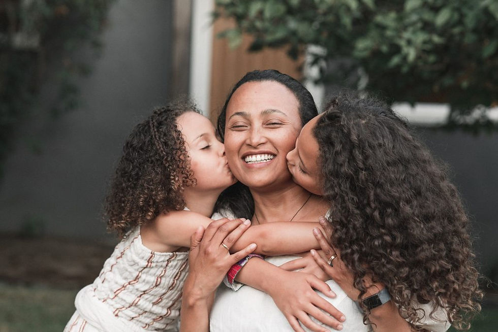 woman in white clothing smiles and is hugged and kissed by two children