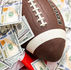 A football on scattered 100-dollar bills with an American flag visible in the background, suggesting a theme of sports and money.