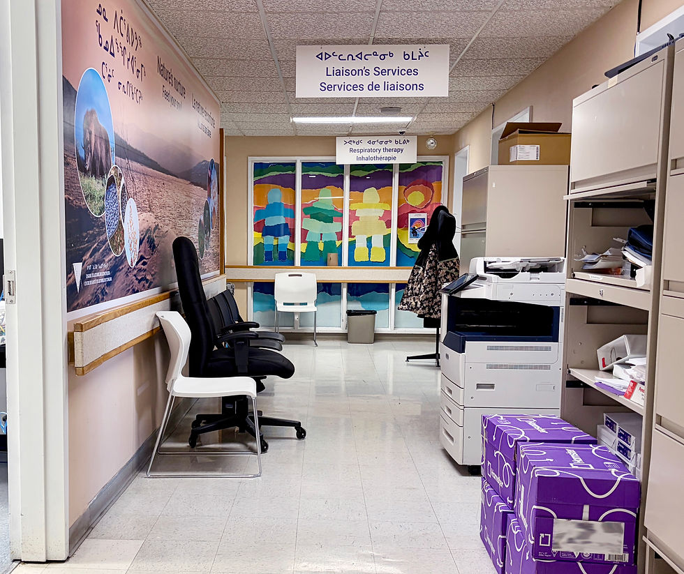 Hospital hallway with signage in English. Inuktitut, and French, chairs, and medical equipment.