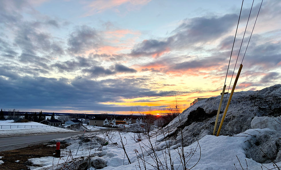 Snow-covered road at sunset with houses in the distance.