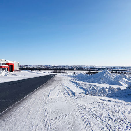 Snow-covered road leading past a building into a wide winter landscape in Kuujjuaq.