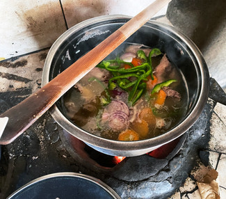 Pot of meat, onions, carrots, and green peppers simmering on a traditional charcoal stove