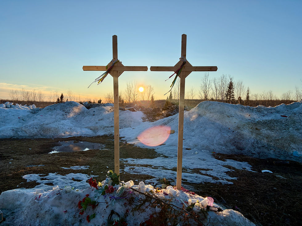 Two wooden crosses by the roadside with flowers placed at their base.
