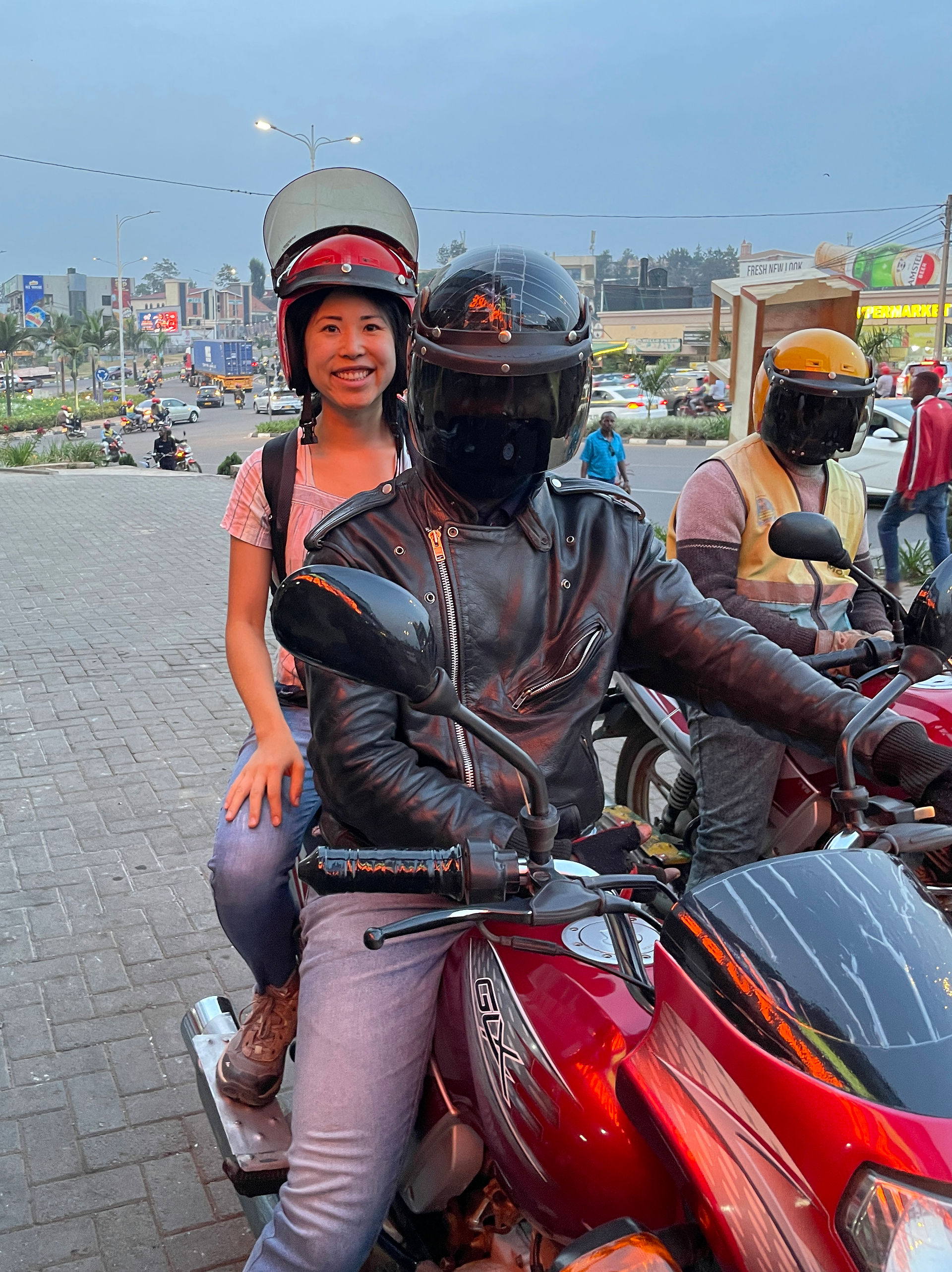 Woman riding on the back of a motorcycle taxi with helmeted drivers in Kigali