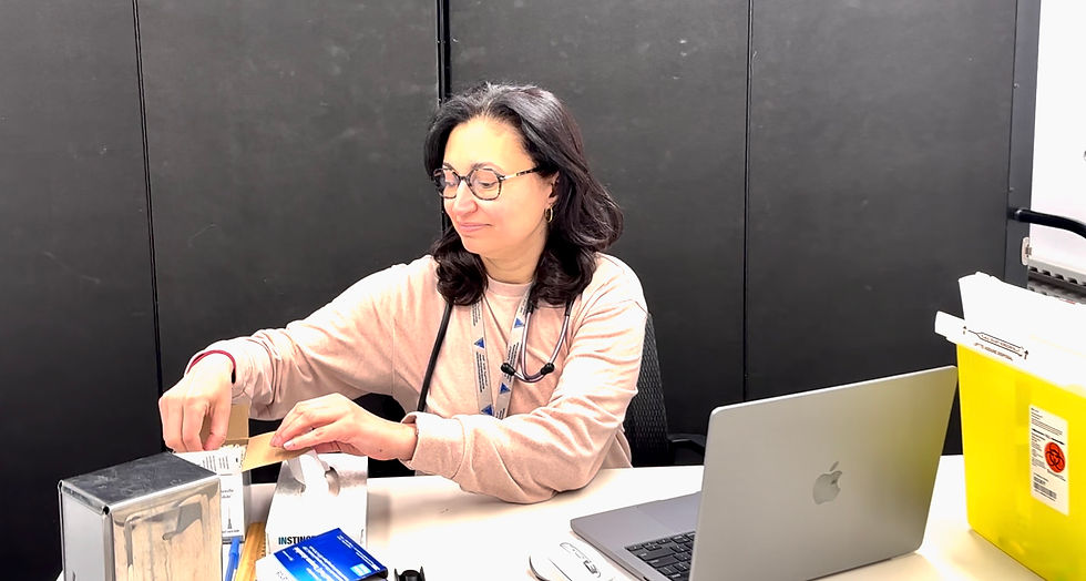 A female doctor wearing glasses and a stethoscope, unpacking boxes at a desk with a laptop and yellow biohazard container.
