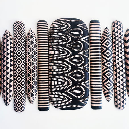 Hand-carved Rwandan wooden panels displayed on a white wall, featuring bold black-and-natural geometric patterns such as zigzags, diamonds, stripes, and interlocking curves