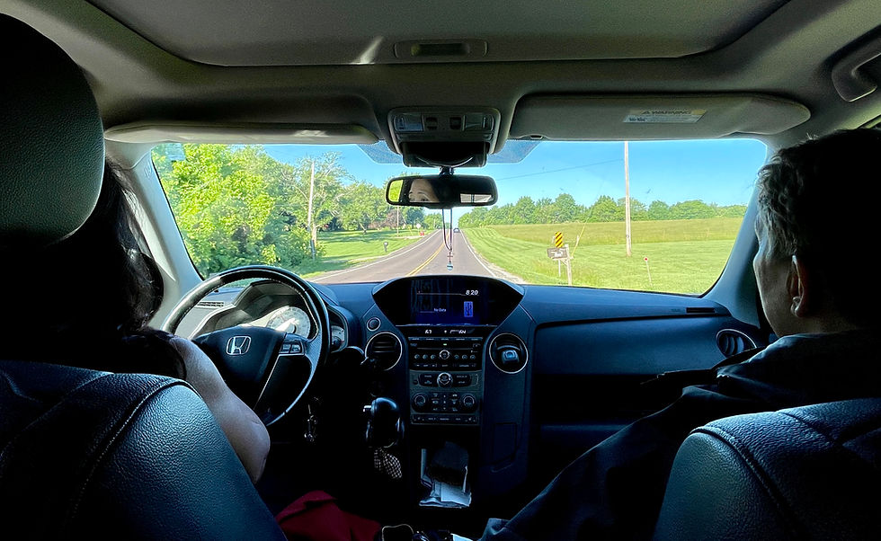 ew from the back seat of a car driving down a quiet rural road, with two people in the front seats