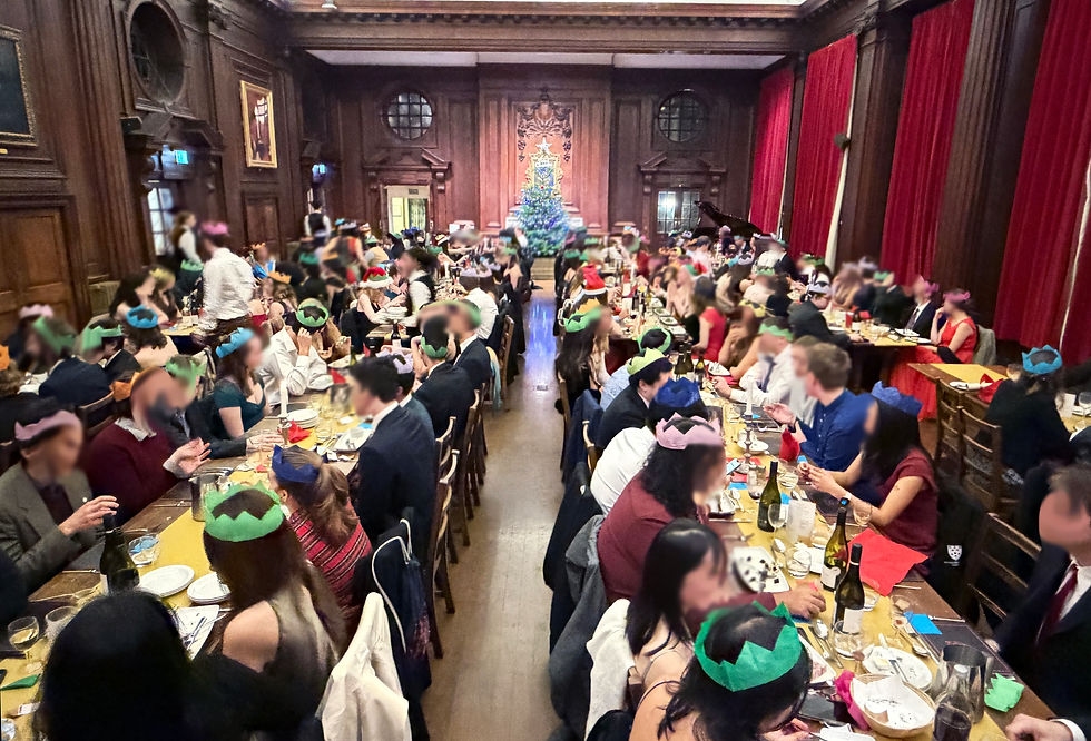 Formal dinner at Lady Margaret Hall with long tables, Christmas decorations, and attendees wearing paper crowns during a festive evening event.