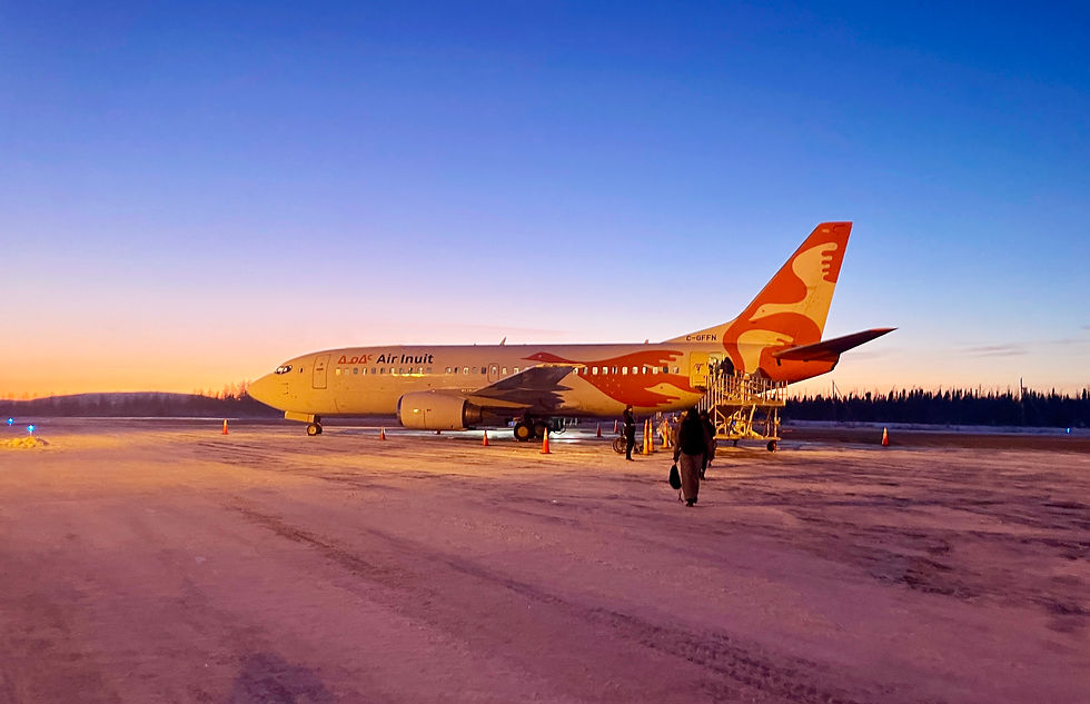 An Air Inuit 737 parked on a snowy runway at sunrise, with a person walking toward the aircraft under a clear blue and orange sky.