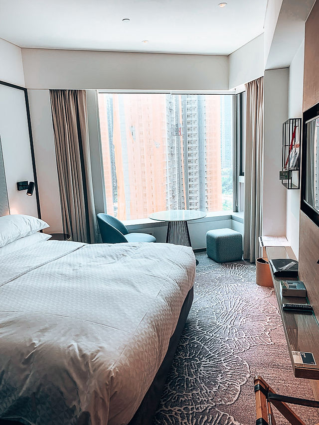 white bed in hotel room with round coffee table near window