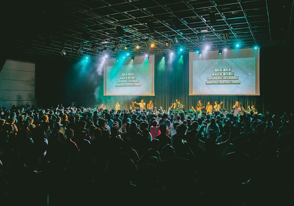 A packed room of young adults worshiping with hands raised before the stage at UNITE Conference 2026 in Yokohama, Japan.