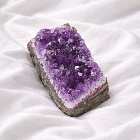 Purple amethyst crystal cluster on white fabric