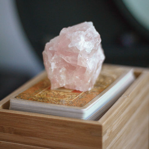 Raw rose quartz crystal on a tarot deck in a wooden box